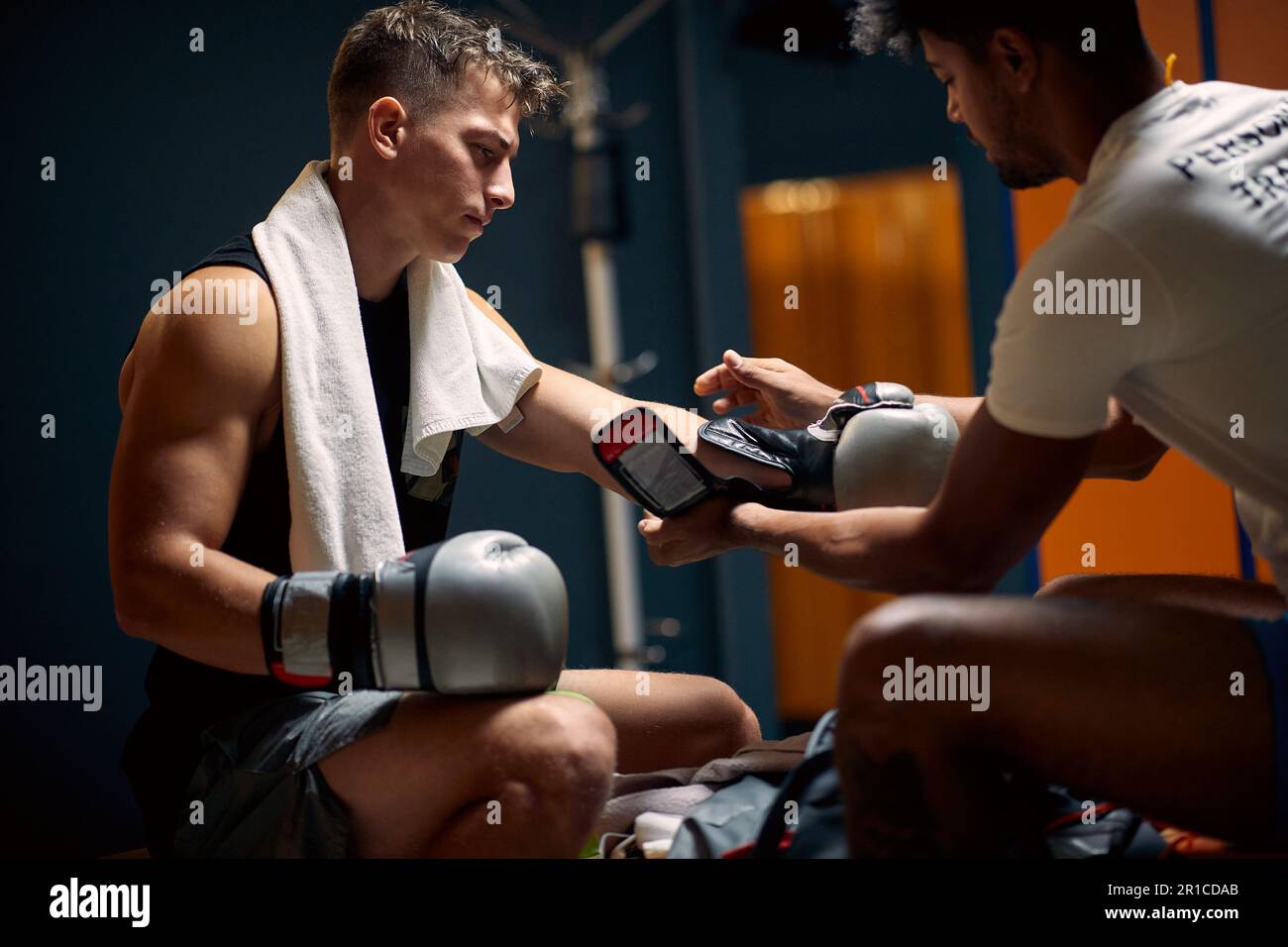 Junger Boxspieler, der sich auf das Boxtraining vorbereitet, der Trainer hilft ihm beim Anziehen von Boxhandschuhen. Sport, Lifestyle, Kampfsport-Konzept. Stockfoto