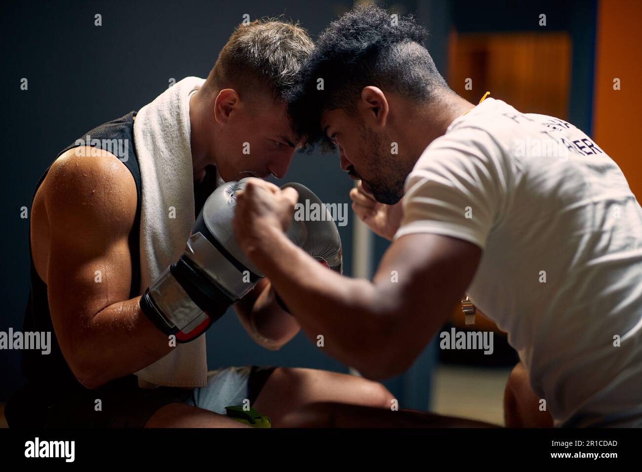 Junger Boxspieler mit Trainer in der Garderobe, der sich auf das Training vorbereitet und die Köpfe gegeneinander hält. Kampfsport, Boxen, Sportkonzept. Stockfoto
