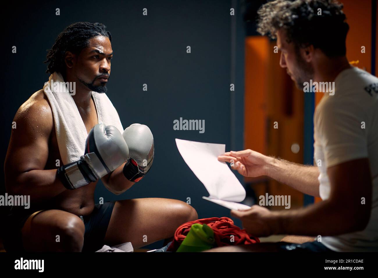 Muskulöser und starker Boxspieler in Schweiß nach dem Workout, der sich von Angesicht zu Angesicht auf der Bank mit seinem Trainer ruht, um Beratung zu erhalten. Sport, Lifestyle-Konz Stockfoto
