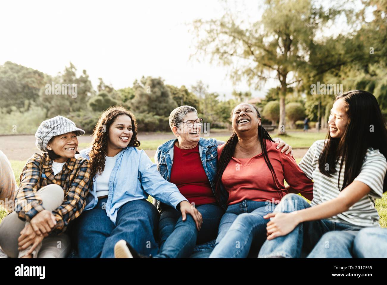 Glückliche Mehrgenerationengruppe von Frauen mit unterschiedlichen ethnischen Zugehörigkeiten, die Spaß haben, in einem öffentlichen Park auf dem Gras zu sitzen - Empowerment-Konzept für Frauen Stockfoto