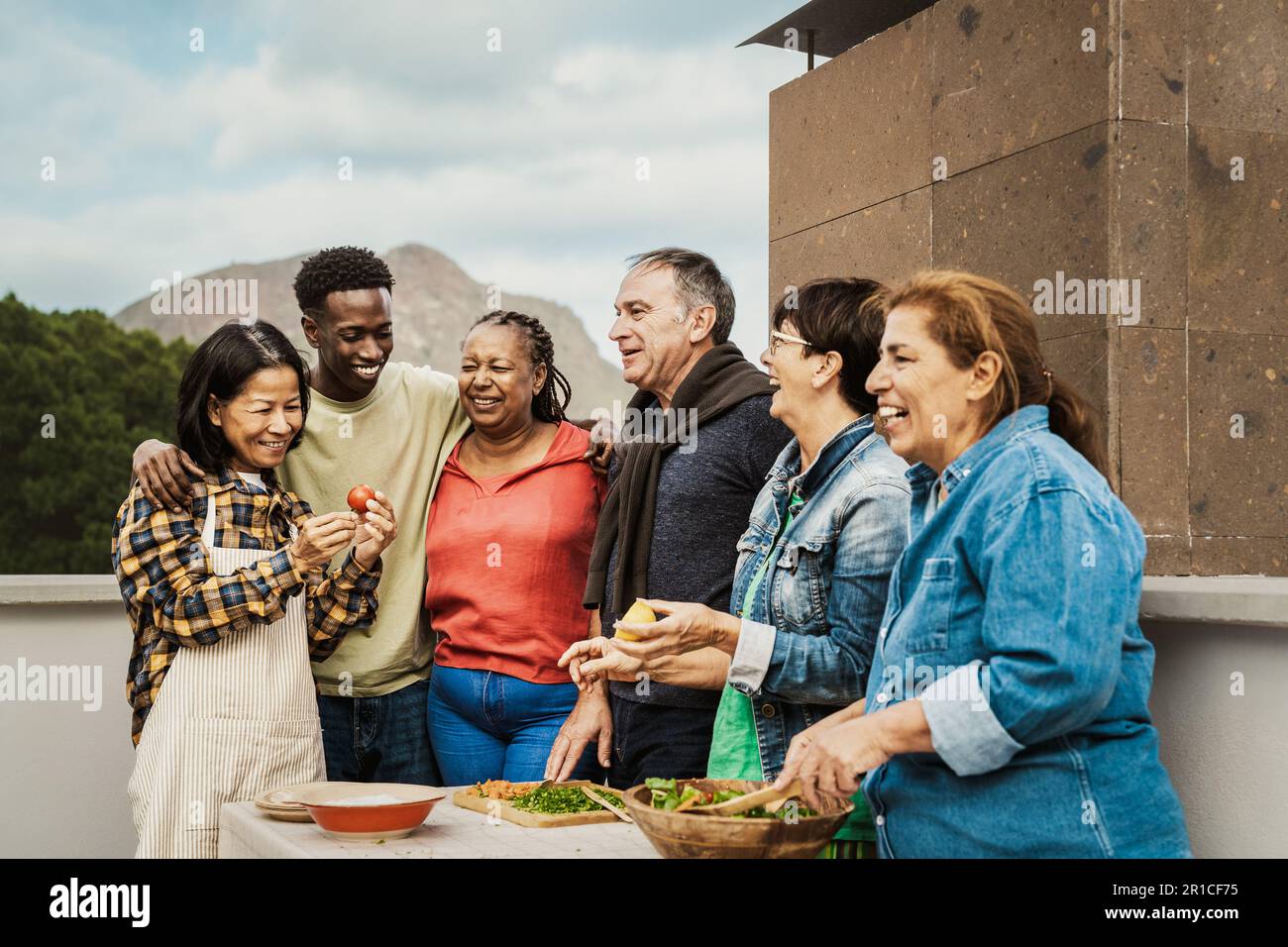 Freunde mehrerer Generationen, die gemeinsam auf dem Dach des Hauses spaßiges Kochen genießen - Zusammenkünfte im Sommer und Essenskonzept Stockfoto