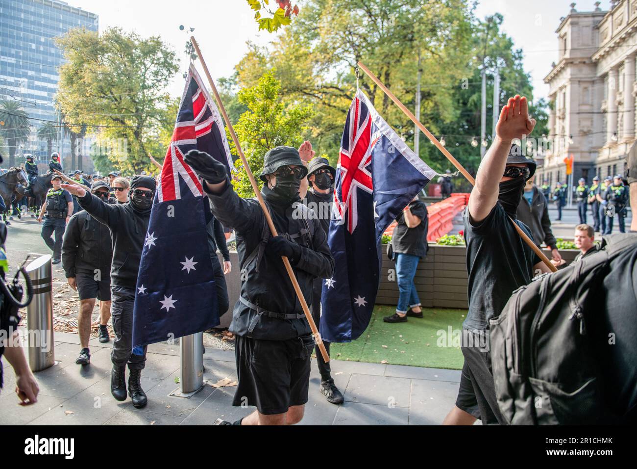 Neonazis-Demonstranten mit Flaggen salutieren, da sie während der Demonstration das Gebiet verlassen sollen. Ein Tag politischer Spannungen und Zusammenstöße entfaltete sich in Melbourne als rechtsextreme Gruppe einer Neonazi-Gruppe, die eine Anti-Einwanderungs-Kundgebung im staatsparlament veranstaltete, und traf auf heftigen Widerstand von linksgerichteten antifaschistischen Gegenprotestierenden. Die Aufruhr-Polizei wurde eingesetzt, als es zwischen den beiden Gruppen zu Schlägereien kam, mit Pfefferspray und Pferden, um die Menge zu kontrollieren. Protestsignale, die Inklusivität, Vielfalt und soziale Gerechtigkeit fordern, wurden in einer Demonstration der Einheit gegen Hassreden und Diskriminierung hoch gehalten. Die Überschneidung Stockfoto