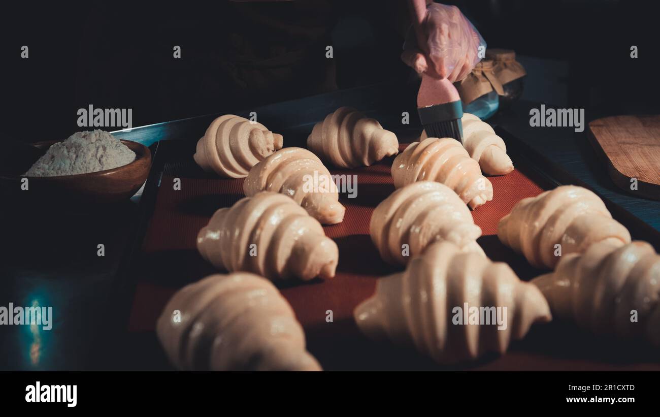 Der Koch schmiert das Eigelb mit wunderschönen Käse-Croissants, bevor er in den Ofen geht Stockfoto