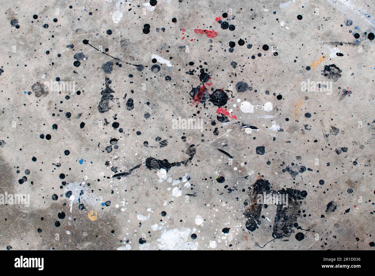 Der Boden ist mit mehreren Tropfen in verschiedenen Farben befleckt. Tropfende Farbe auf dem Betonboden wunderschöne Kunst. Tröpfchen mit roten, schwarzen und weißen Flecken Stockfoto