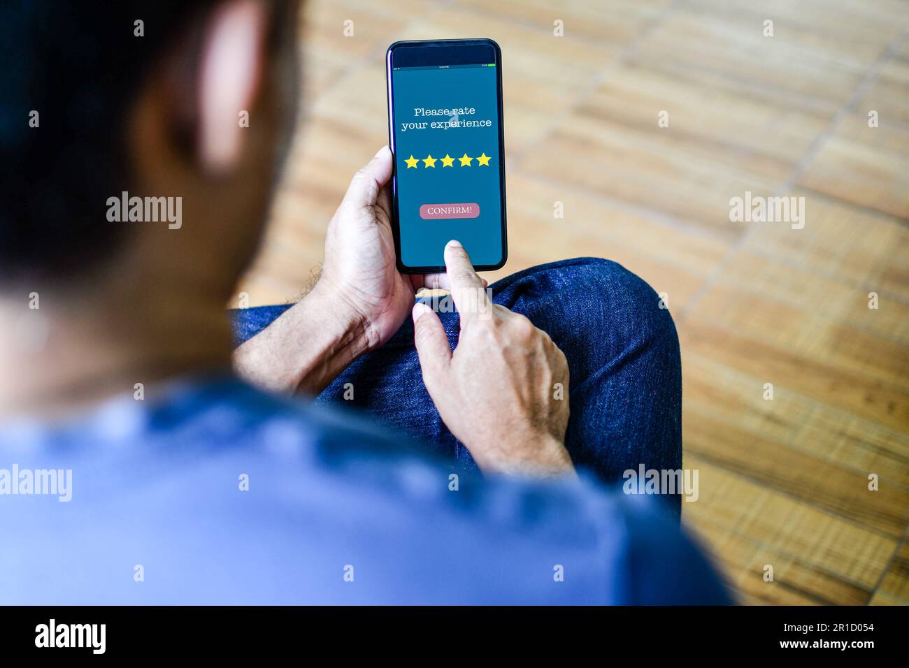 Der Smartphone-Bildschirm zeigt die Meldung Bitte bewerten Sie Ihre Erfahrung an, um die Zufriedenheit mit dem Service zu bestätigen. Der Mann sitzt und hält sein Smartphone, um zu Hause zu arbeiten. Konz Stockfoto