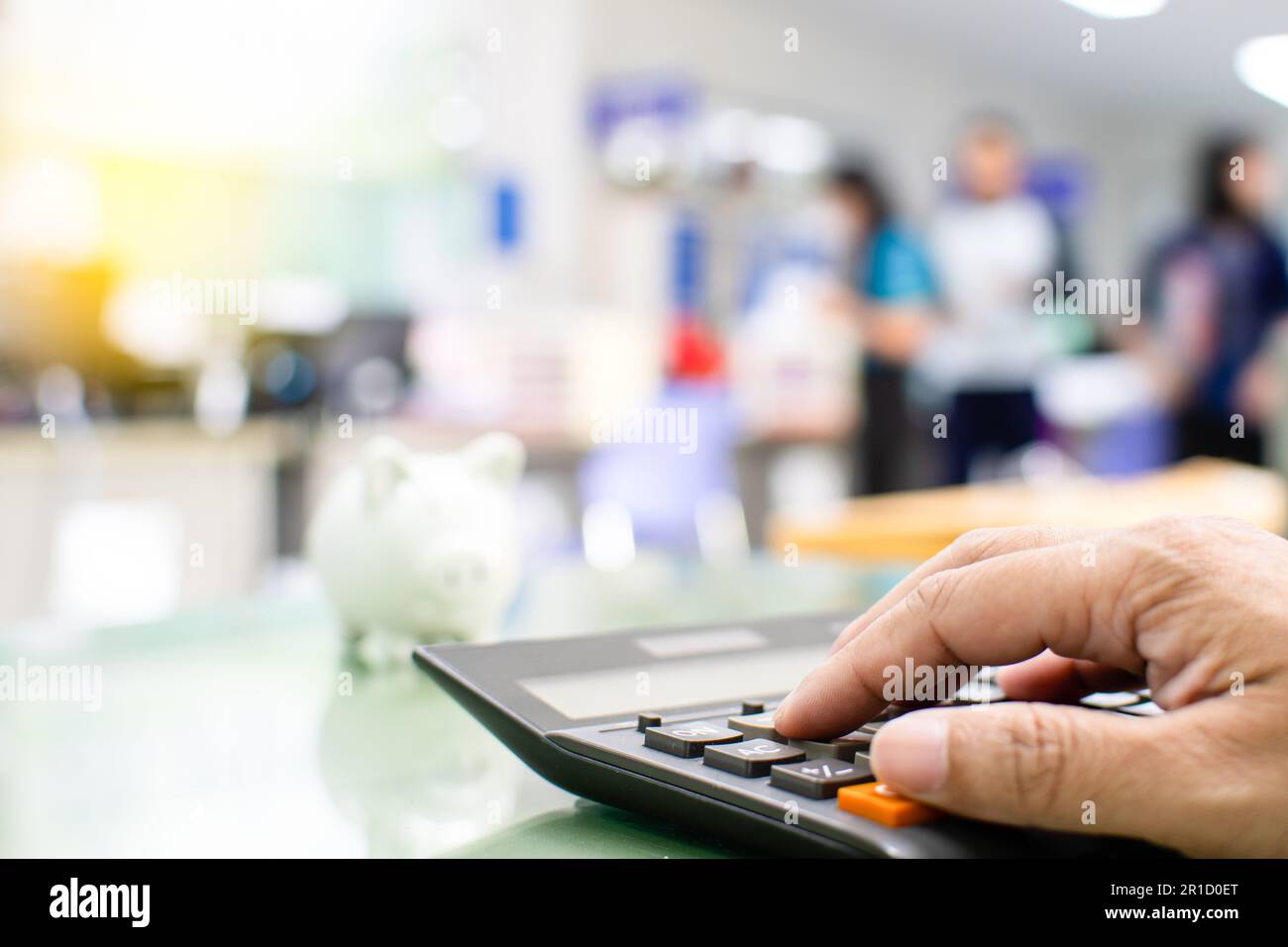 Nahaufnahme eines männlichen Fingers, der einen Taschenrechner auf einen gläsernen Schreibtisch in einem Büro drückt, um die Bankzinsen für Kunden zu berechnen, die einen Kredit benötigen, verschwommenes Weiß Stockfoto