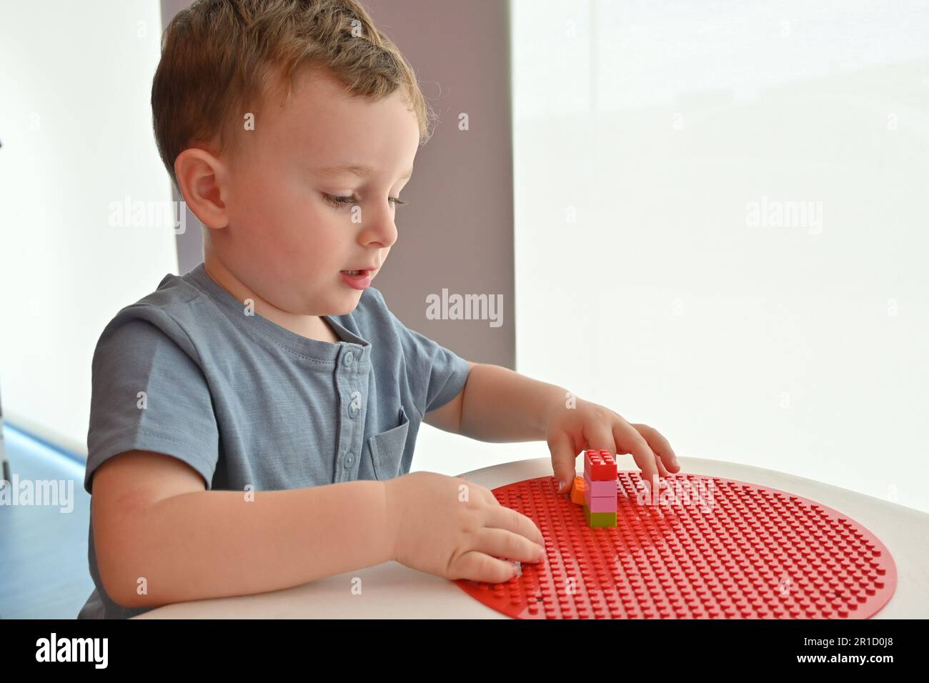 Kleines Kind spielt mit vielen bunten Plastikspielzeugen im Innenbereich und baut verschiedene Autos und Gegenstände. Stockfoto