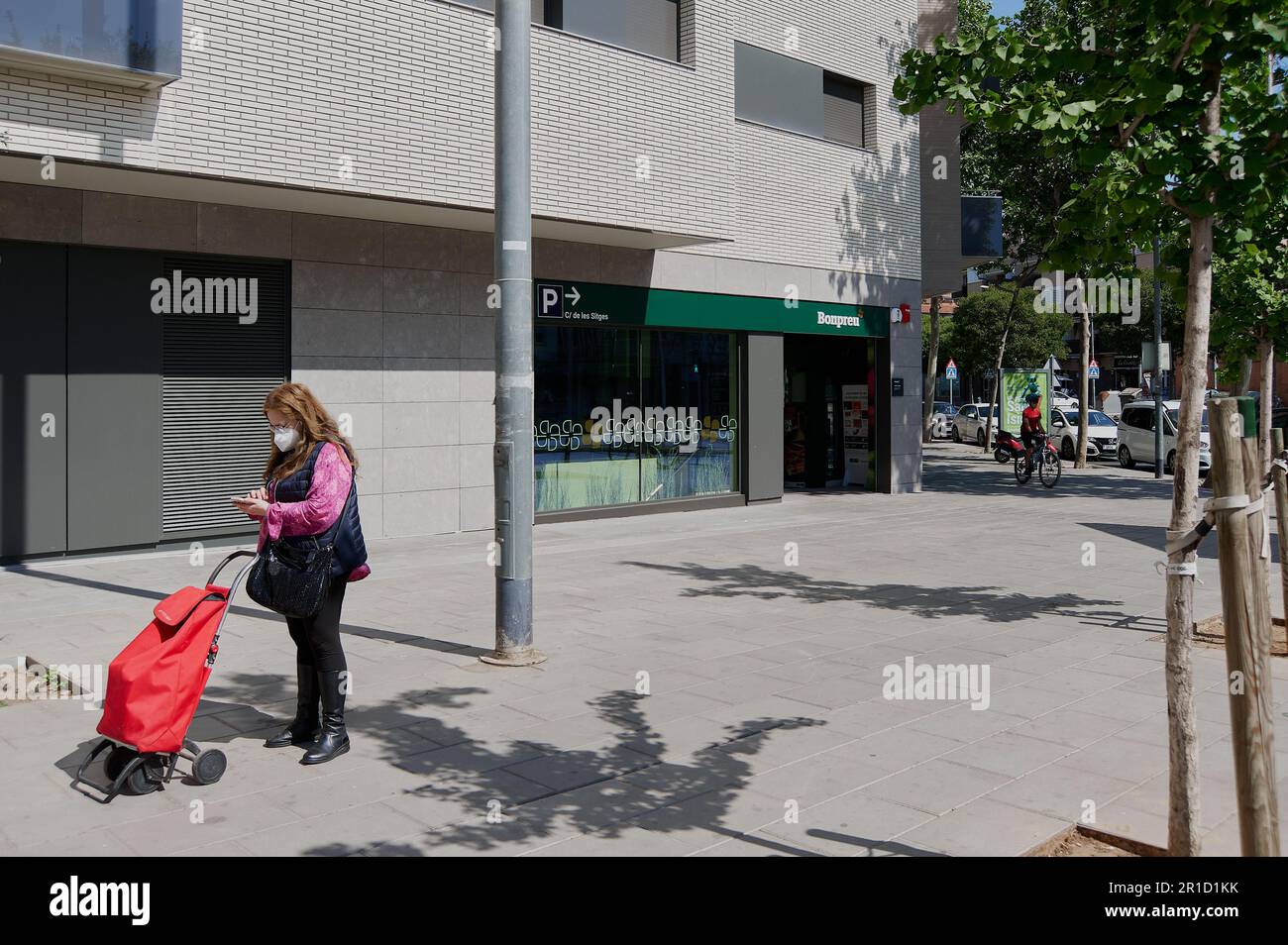 Viladecans - 13. Mai 2023: Lady schaut auf ihr Handy, wenn sie mit einem Radfahrer im Hintergrund im Supermarkt einkaufen geht. Stockfoto
