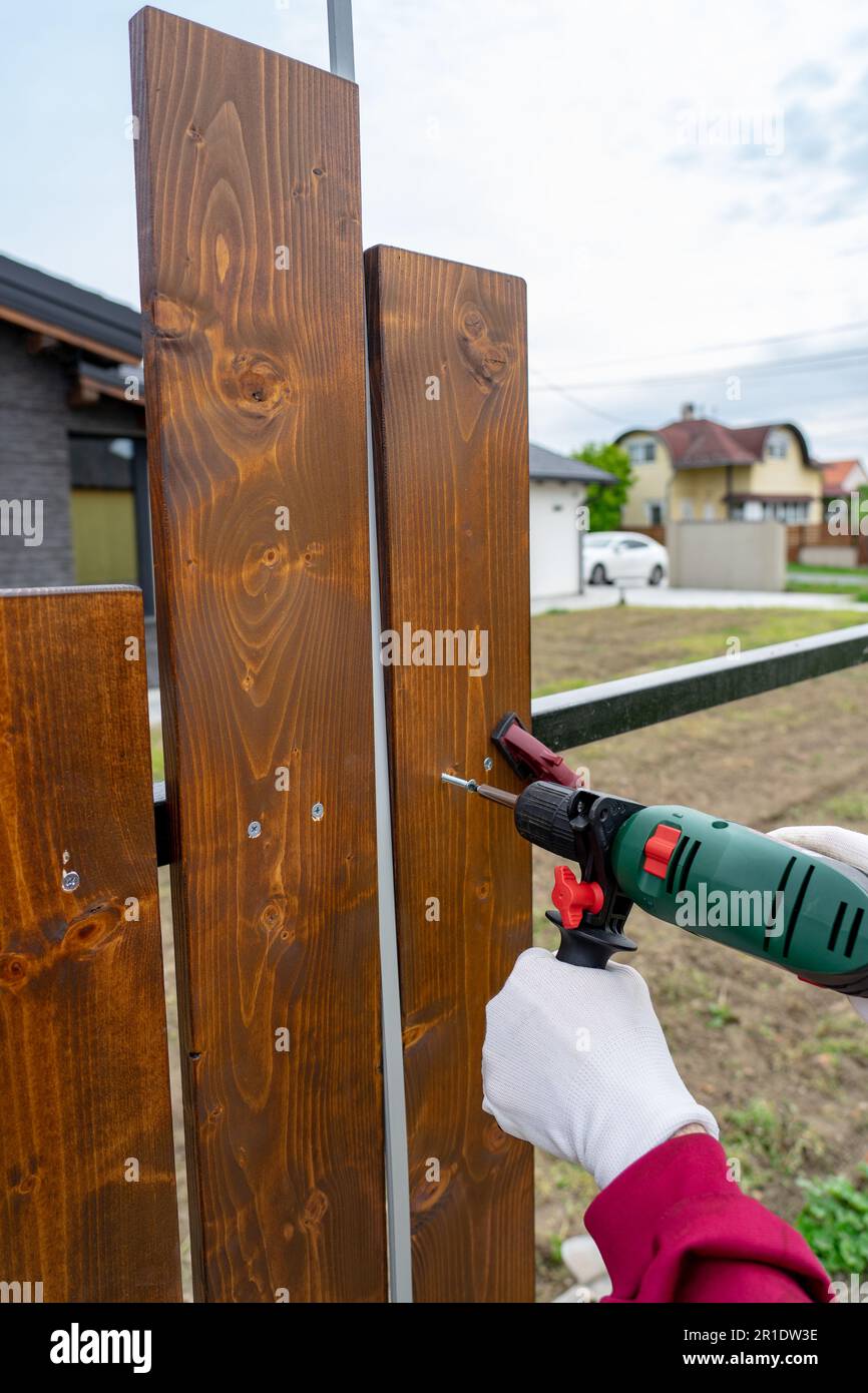 Ein Mann baut seinen eigenen speziellen Holzzaun mit Bohrmaschine. Stockfoto