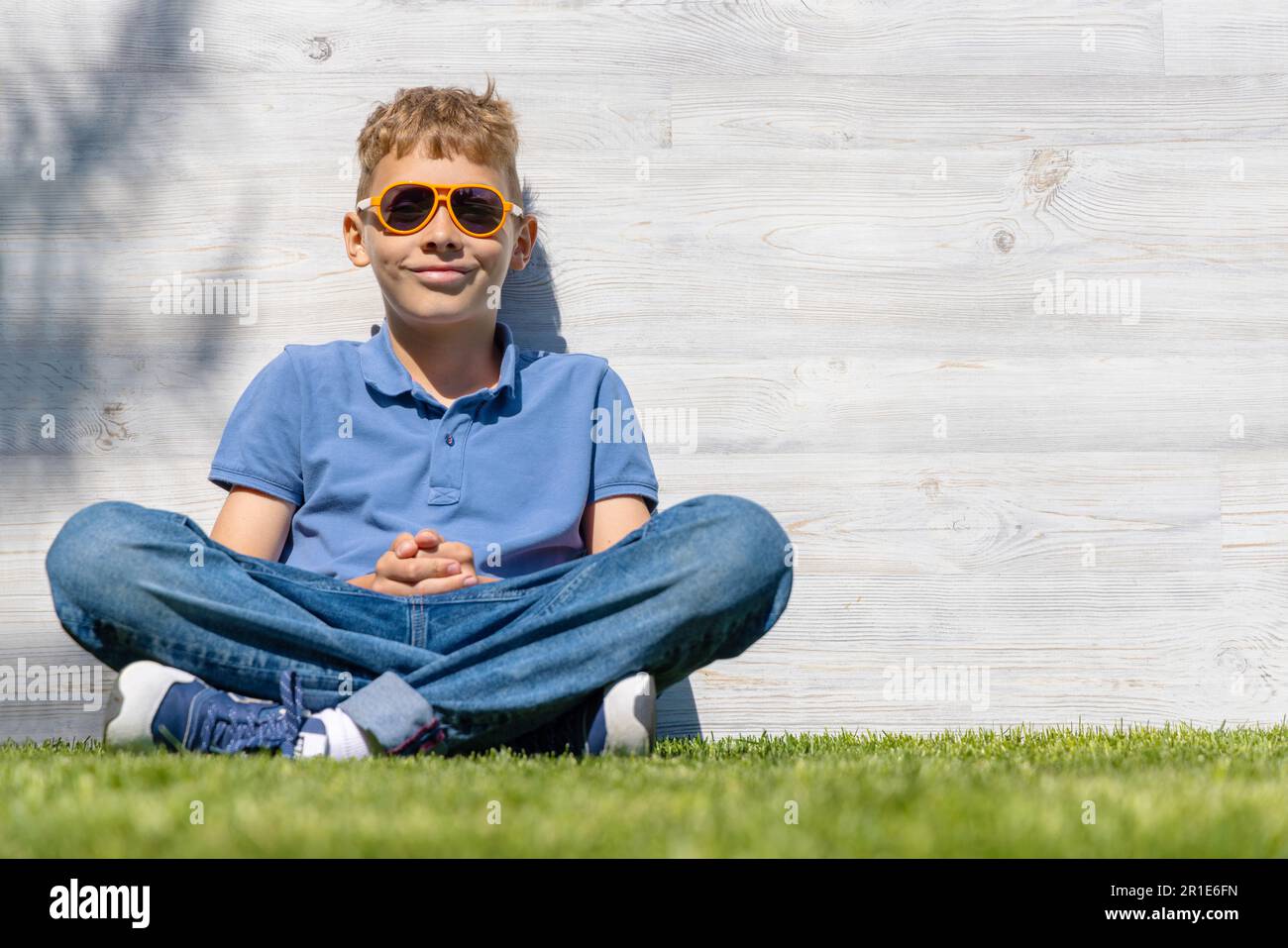Ein Schuljunge mit Sonnenbrille, der auf einem grasbedeckten Feld sitzt. Mit Kopierbereich Stockfoto Ein Schuljunge mit Sonnenbrille, der auf einem grasbedeckten Feld sitzt. Mit Kopierbereich Stockfoto