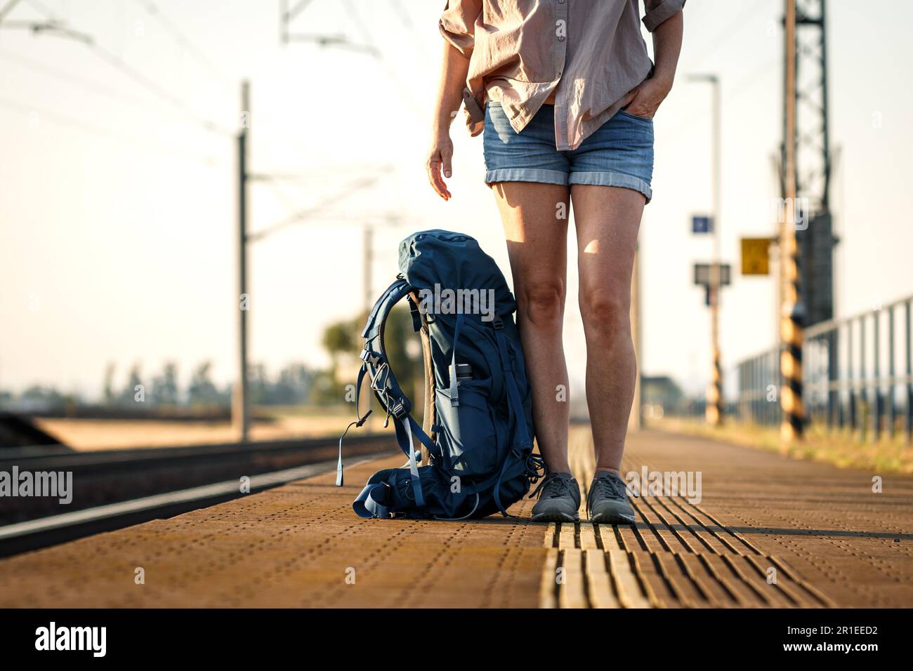 Ein Zugreisender mit Rucksack wartet am Bahnhofsplatz. Eine Frau, die allein im Sommerurlaub unterwegs ist Stockfoto