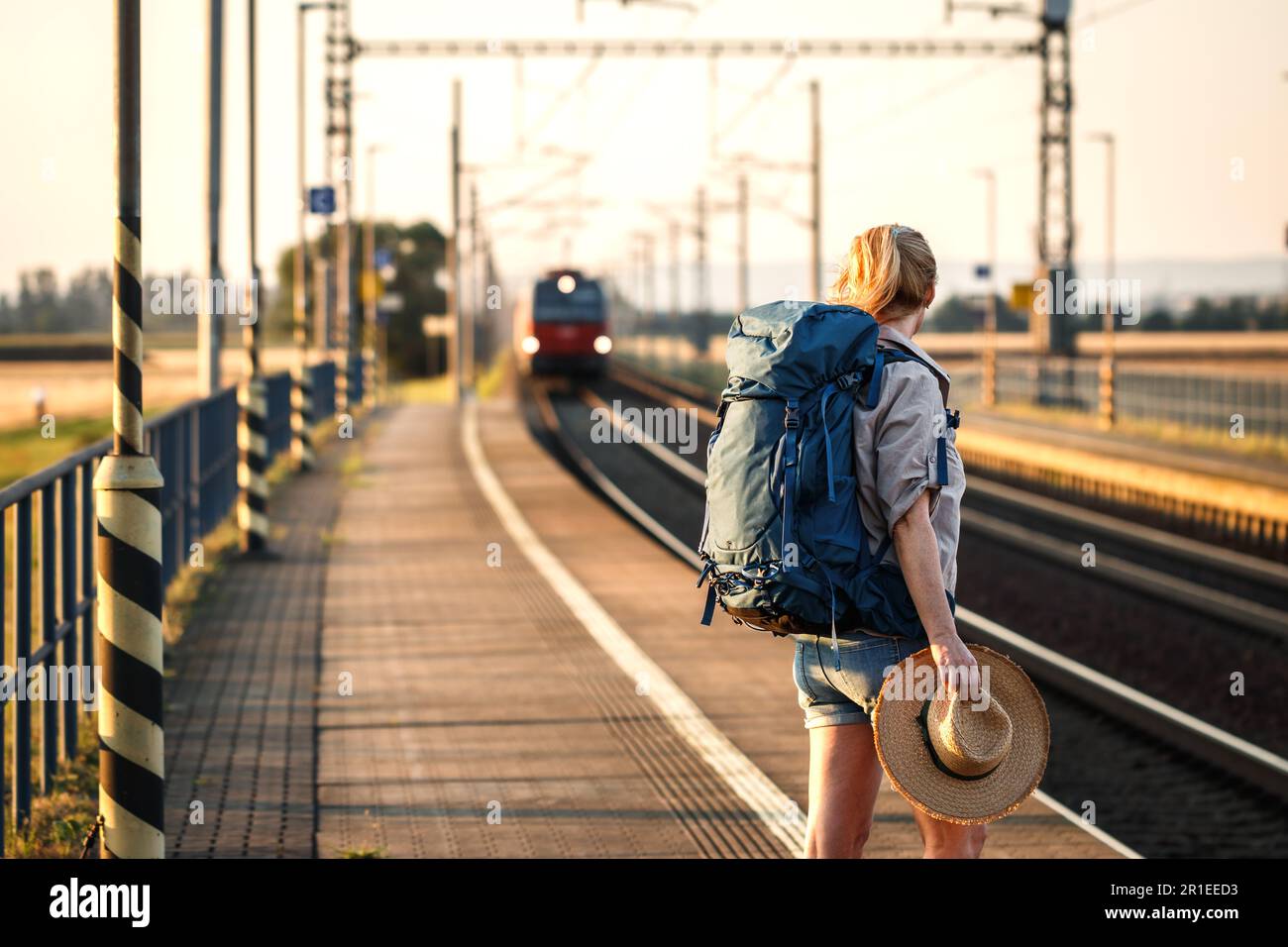 Reisender mit Rucksack, der am Bahnhofsplatz steht und den ankommenden Zug betrachtet Stockfoto