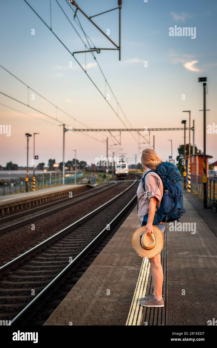 Eine Reisende, die während des Sonnenuntergangs am Bahnhof wartet. Alleinreisende sind bereit für die Sommerreise Stockfoto