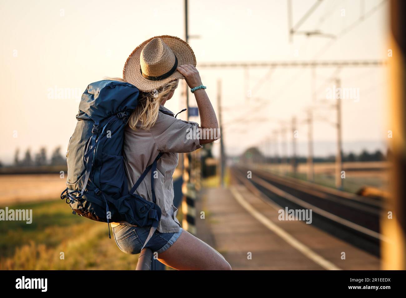 Ein Zugreisender mit Rucksack und Hut wartet am Bahnhofsplatz. Eine Frau, die allein im Urlaub ist Stockfoto