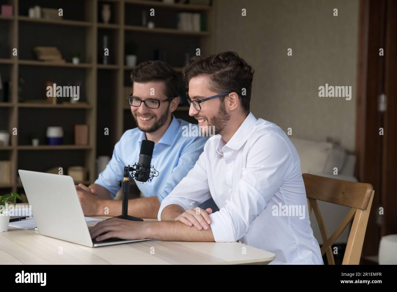 Fröhliche zwei Männer sitzen am Laptop und Studio-Mikrofon Stockfoto