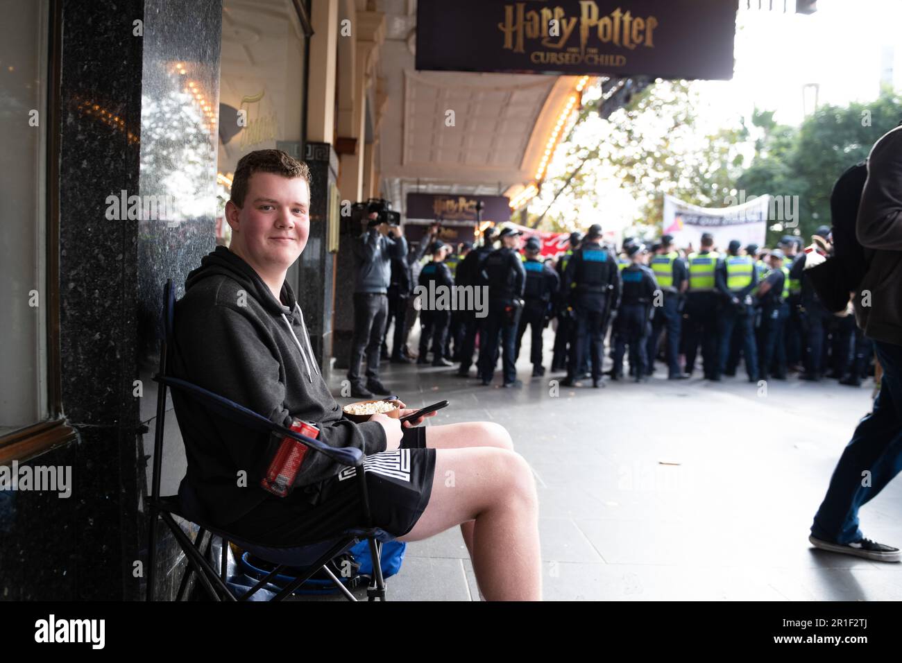 Melbourne, Australien, 13. Mai 2023. Ein junger Mann sitzt und isst Popcorn, während die Polizei die beiden Gruppen während einer hitzigen politischen Kundgebung gegen Rassismus auseinanderhält, während rechtsextreme Neonazi-Gruppen eine Demonstration im staatsparlament abhielten, die am 13. Mai 2023 in Melbourne, Australien, zu Zusammenstößen und Schikanen führte. Kredit: Michael Currie/Speed Media/Alamy Live News Stockfoto