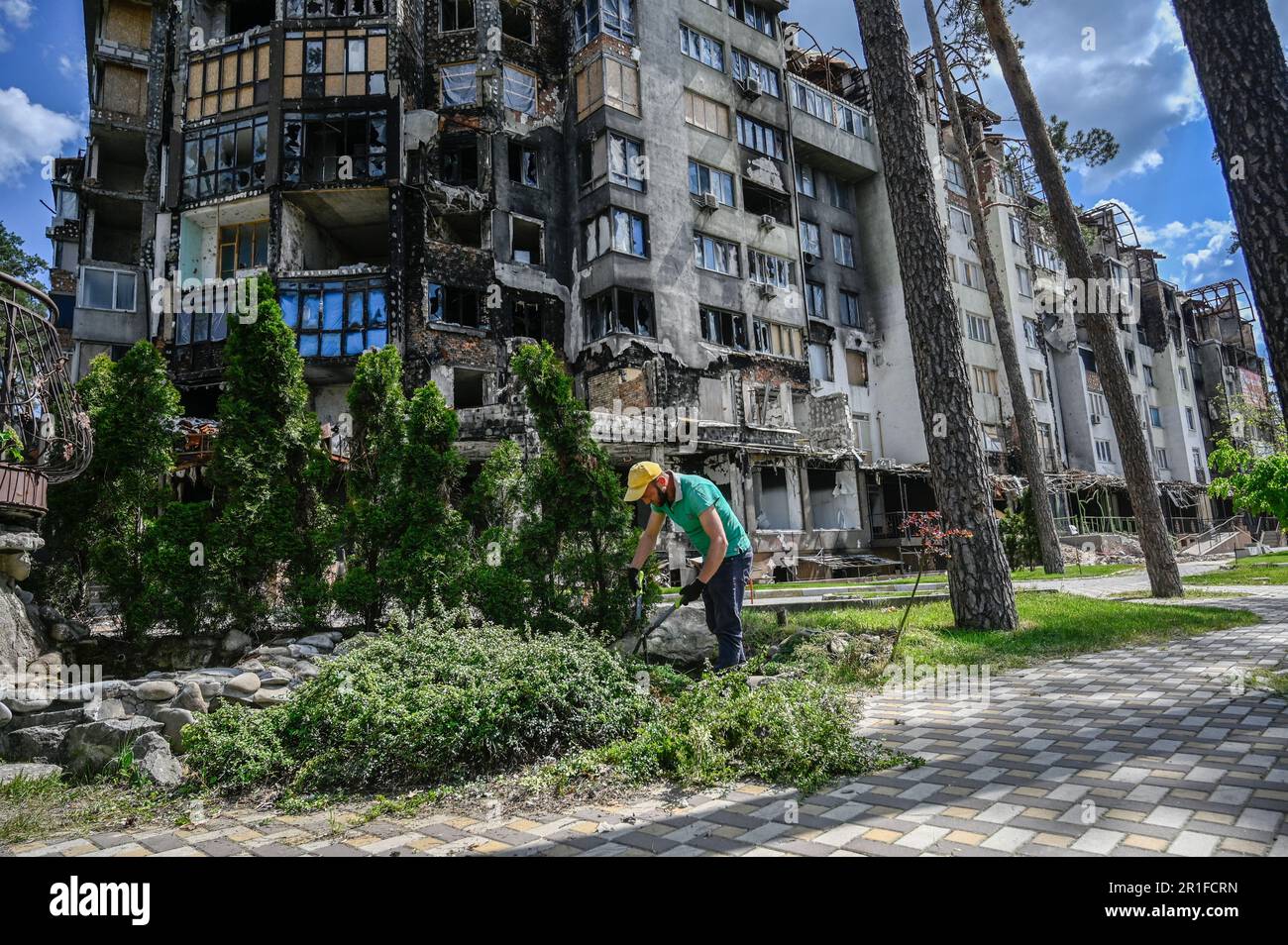 Irpin, Ukraine. 13. Mai 2023. Ein Einheimischer schneidet Büsche in der Nähe eines schwer beschädigten Wohngebäudes ab, das infolge der Invasion der russischen Armee in der Ukraine beschädigt wurde. Russland marschierte am 24. Februar 2022 in die Ukraine ein und löste damit den größten militärischen Angriff in Europa seit dem Zweiten Weltkrieg aus Kredit: SOPA Images Limited/Alamy Live News Stockfoto