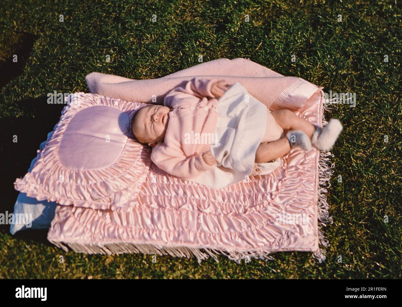 Kleines Mädchen, das auf einer rosa Decke auf Gras liegt. 1950er Stockfoto