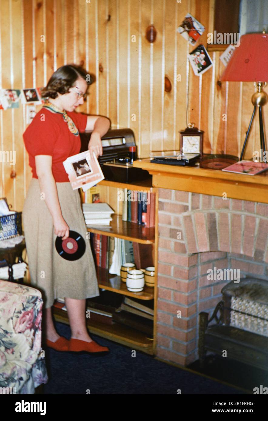 Junge Frau mit einer 45-U/min-Platte, die sich darauf vorbereitet, sie auf einen Plattenspieler zu stellen. 1953 Stockfoto