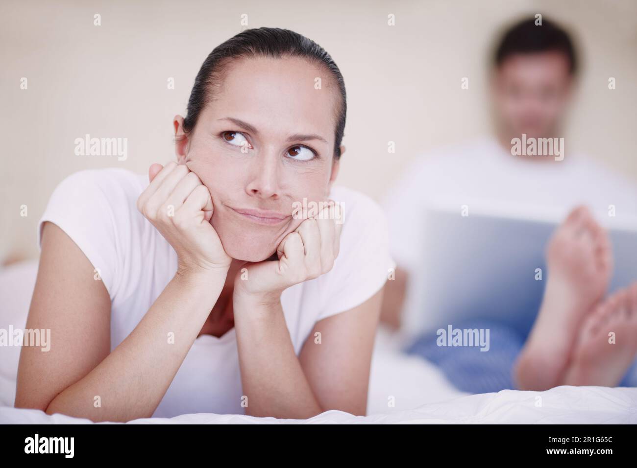 Er ist so egoistisch. Eine junge Frau, die verärgert von ihrem Mann aussieht, der im Hintergrund mit einem Laptop sitzt. Stockfoto