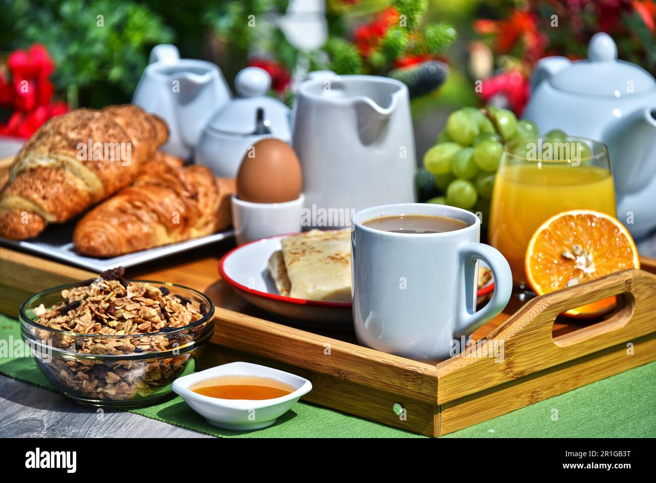 Frühstück serviert mit Kaffee, Orangensaft, Croissants, Müsli und Obst im Garten Stockfoto