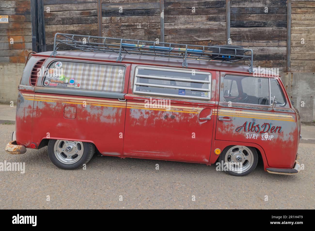 Rayleigh, Großbritannien. Mai 2023. Ein verwitterter roter Volkswagen Typ 2-Van mit Surf-Shop-Branding steht auf einer Straße in Rayleigh, Essex. Der Van verfügt über spezielle Räder, eine abgesenkte Federung, einen Dachträger und Vorhangfenster, die an Surfkultur und Nomadenreisen erinnern. Farm Fresh Garage Truck und amerikanische Fahrzeuge werden gezeigt. Penelope Barritt/Alamy Live News Stockfoto