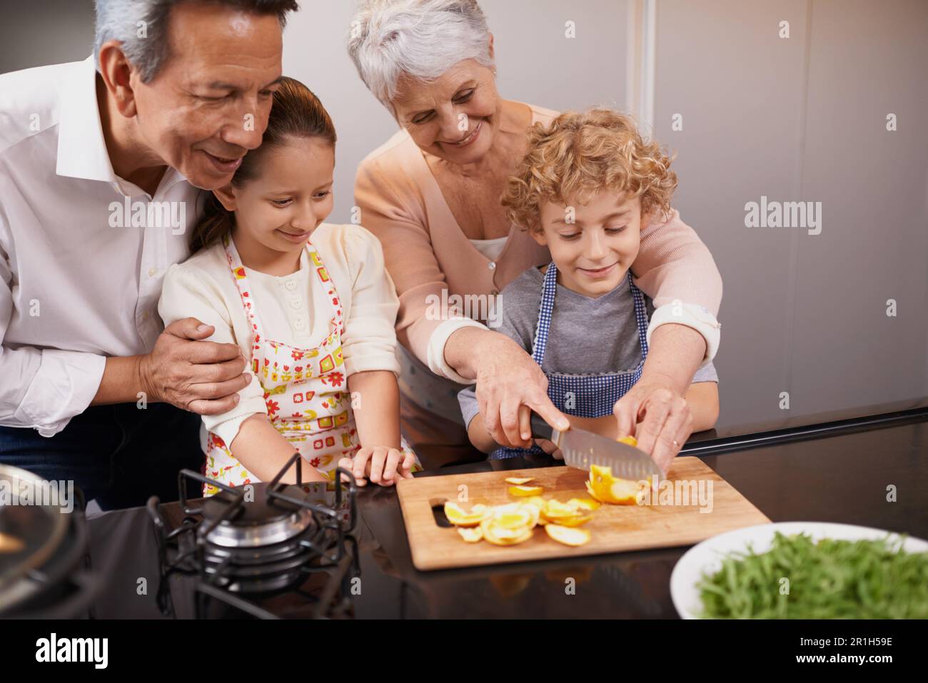 Essen, glückliche Kinder oder Großeltern, die Kochkünste für ein gesundes Abendessen mit Obst oder Gemüse zu Hause lehren. Kinder lernen, Messer oder Stockfoto