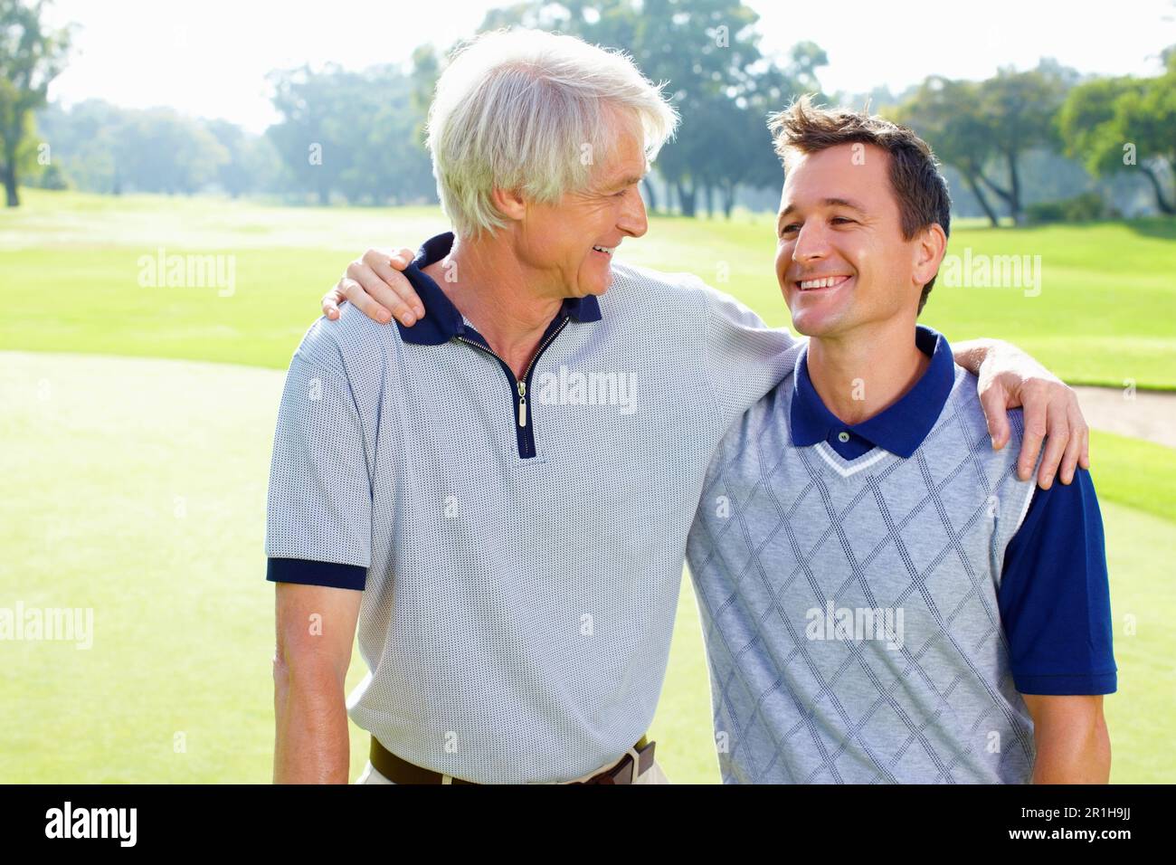 Vater und Sohn lächeln und sehen sich an. Porträt von Vater und Sohn auf dem Golfplatz, die lächeln und sich ansehen. Stockfoto