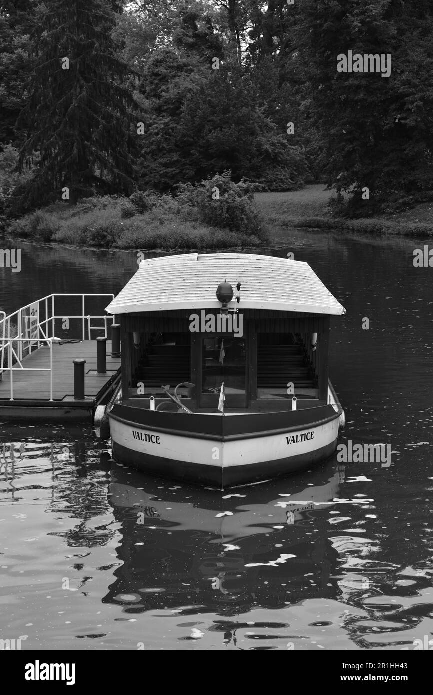 Eine Graustufe einer ruhigen Szene eines kleinen Bootes namens „Valtice“, das an einem hölzernen Pier angelegt ist Stockfoto