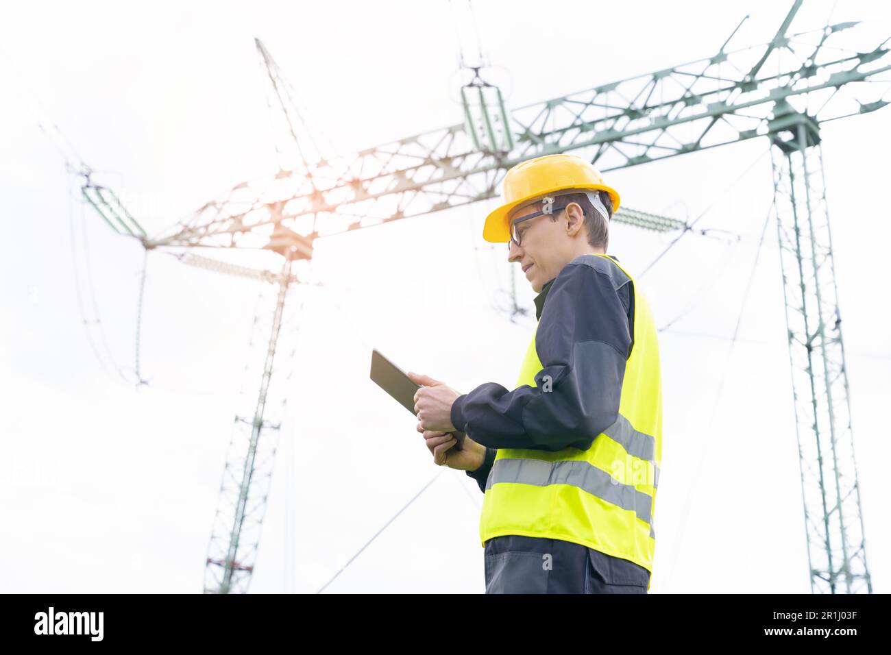 Ingenieur mit digitalem Tablet auf dem Hintergrund eines Stromleitungsturms. Hochwertiges Foto Stockfoto