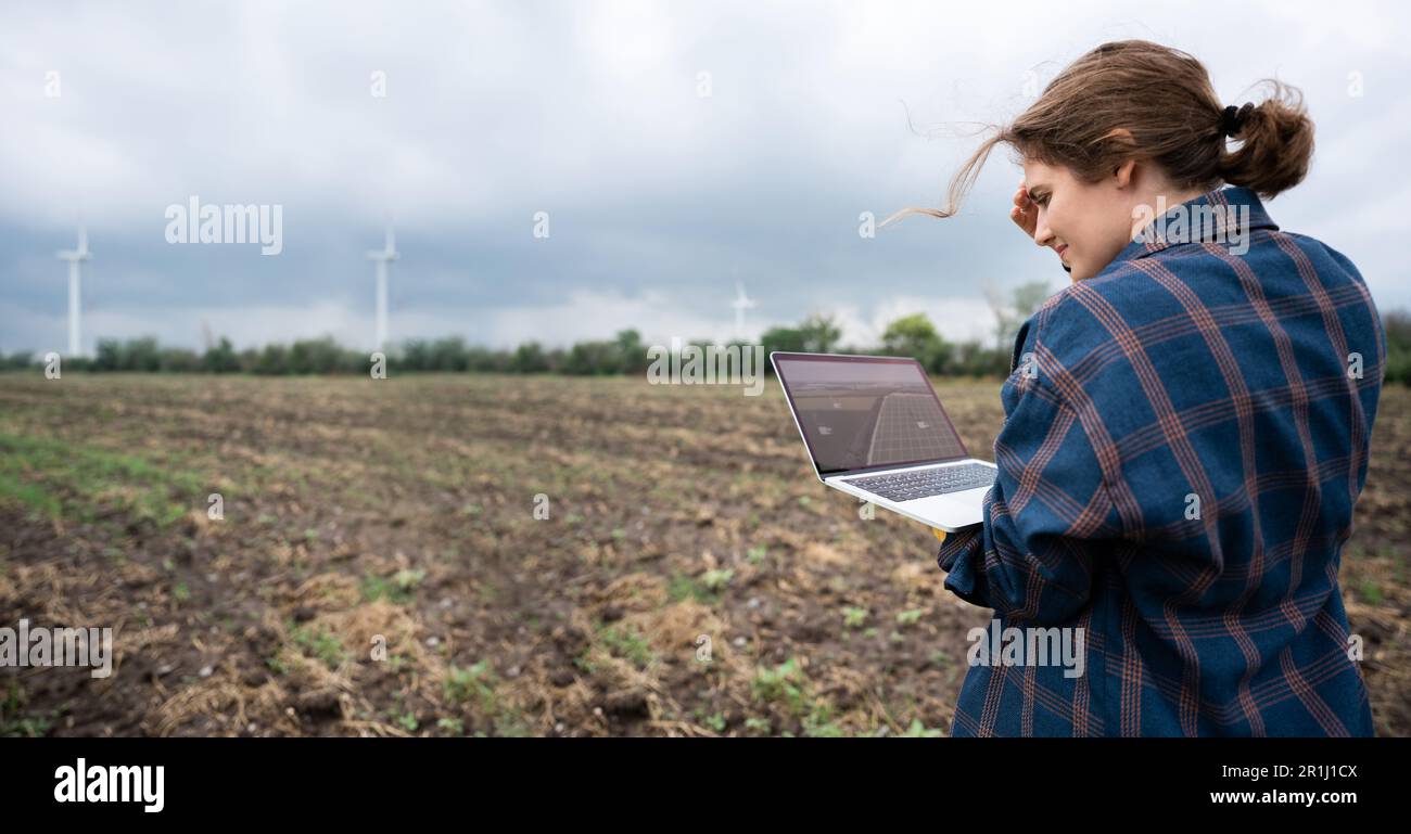 Bauer mit Laptop auf dem Feld. Windturbinen am Horizont. Intelligente, nachhaltige Landwirtschaft und Digitalisierung der Landwirtschaft. Hochwertiges Foto Stockfoto