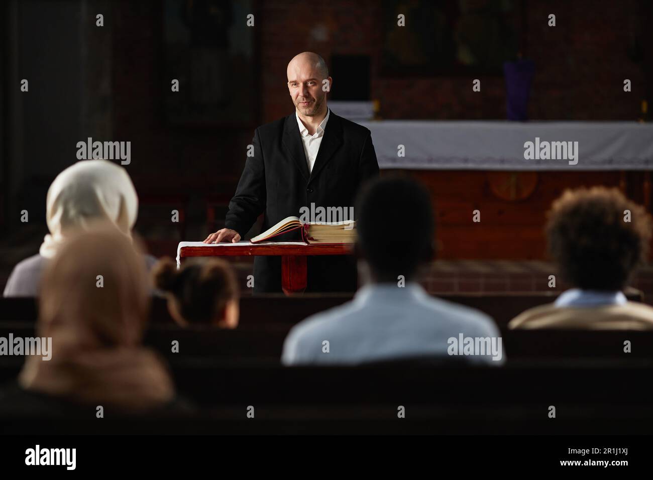 Reifer Prediger, der vor dem Altar steht, mit der Bibel und Gebete für die Menschen in der Kirche liest Stockfoto