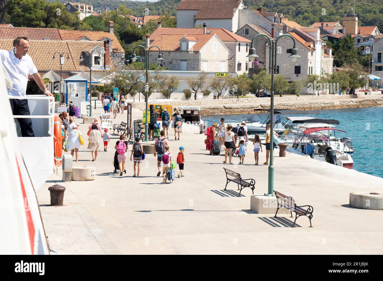 Insel Zlarin, Kroatien - 22. Juli 2022: Menschen verlassen den Pier und ein Mann, der auf einer Jadrolinija-Fähre arbeitet und vom Deck aus beobachtet Stockfoto