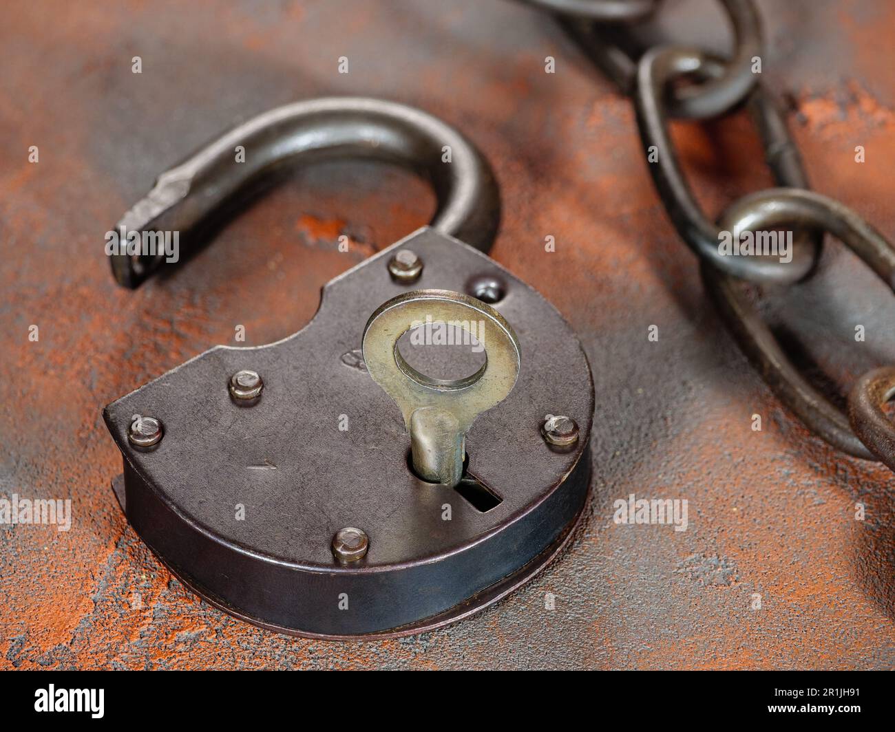 Öffnen Sie das Vorhängeschloss mit dem Schlüssel und einer alten rostigen Gliederkette auf grunge-orangefarbenem Hintergrund Stockfoto