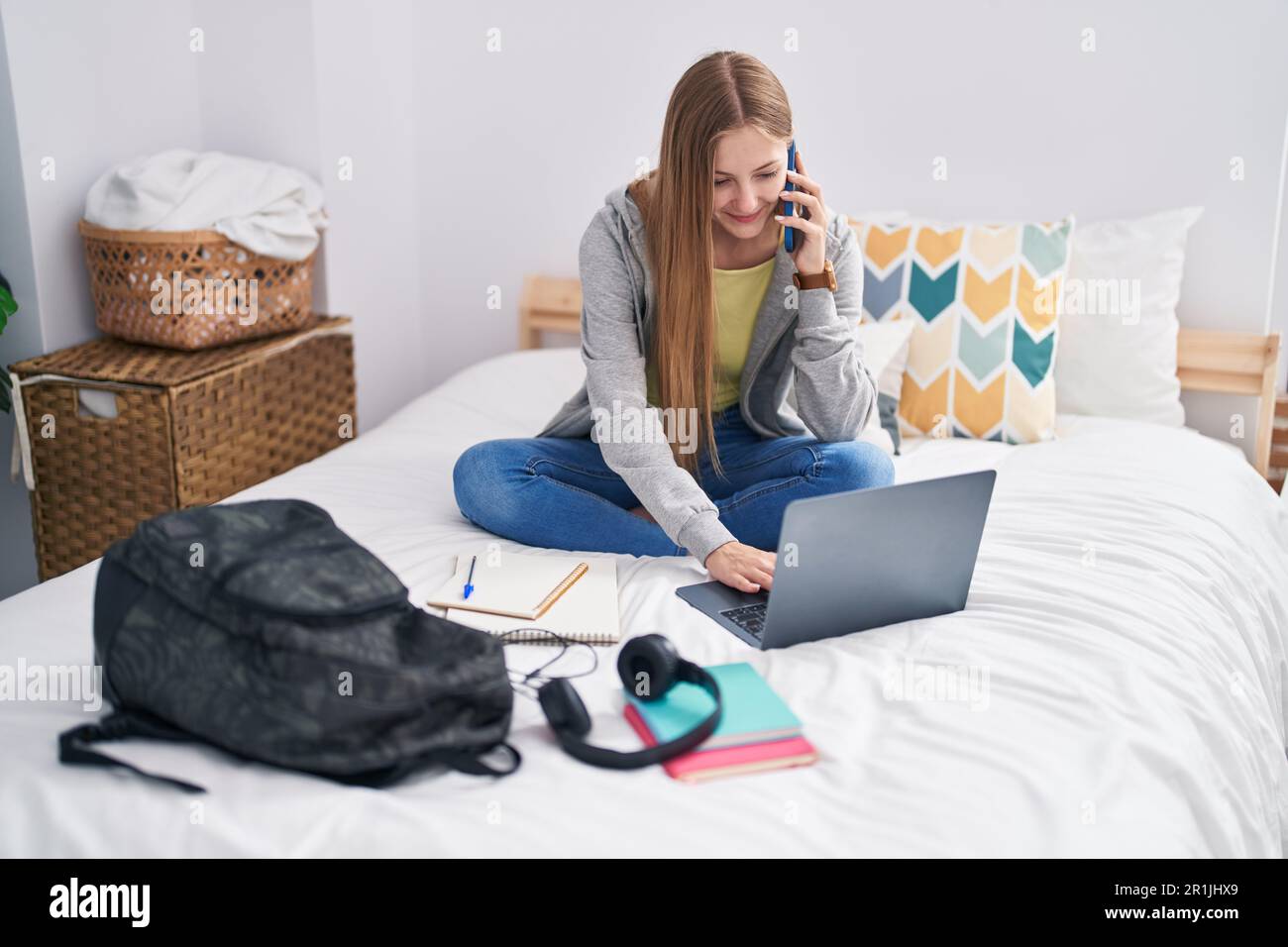 Junge kaukasische Frau, die im Schlafzimmer mit einem Laptop auf dem Smartphone spricht Stockfoto