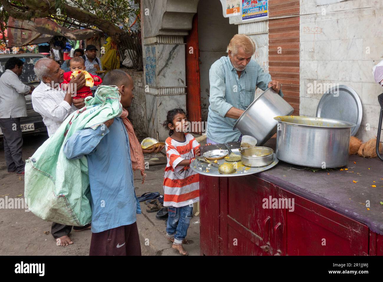 Ein Mädchen, das auf kostenloses Essen wartet, das von einer Wohltätigkeitsangestellten in Paharganj, Neu-Delhi, Indien, verteilt wird Stockfoto