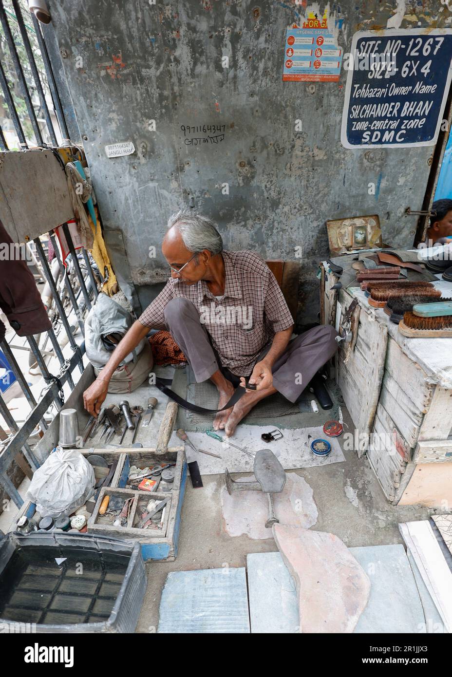Indischer Schuhmacher in Straßenwerkstätten, der Gürtel repariert, in Delhi, Indien Stockfoto