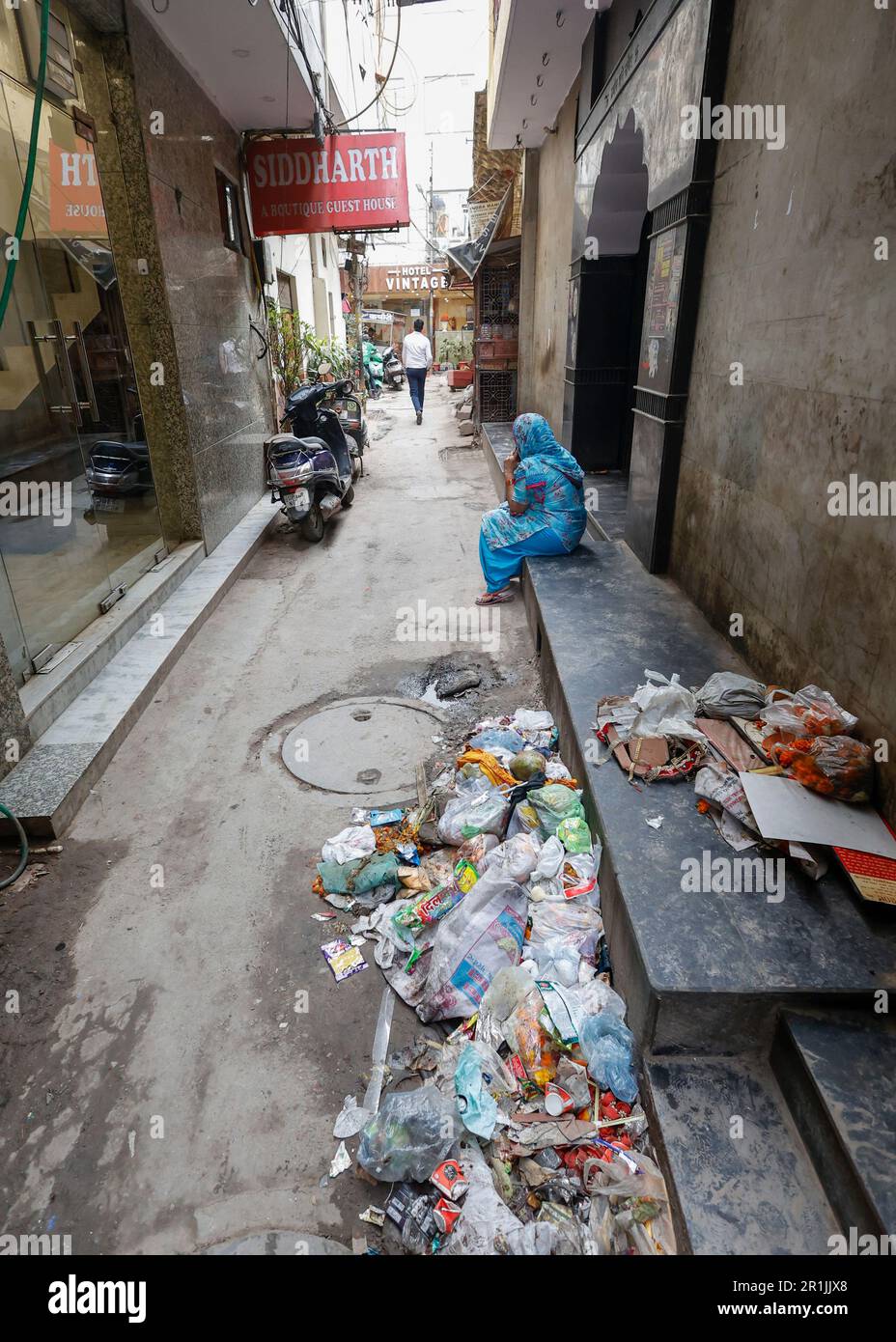 Frau sitzt auf der Tempeleingangstreppe in einer schmutzigen Gasse in Paharganj, Neu-Delhi, Indien Stockfoto