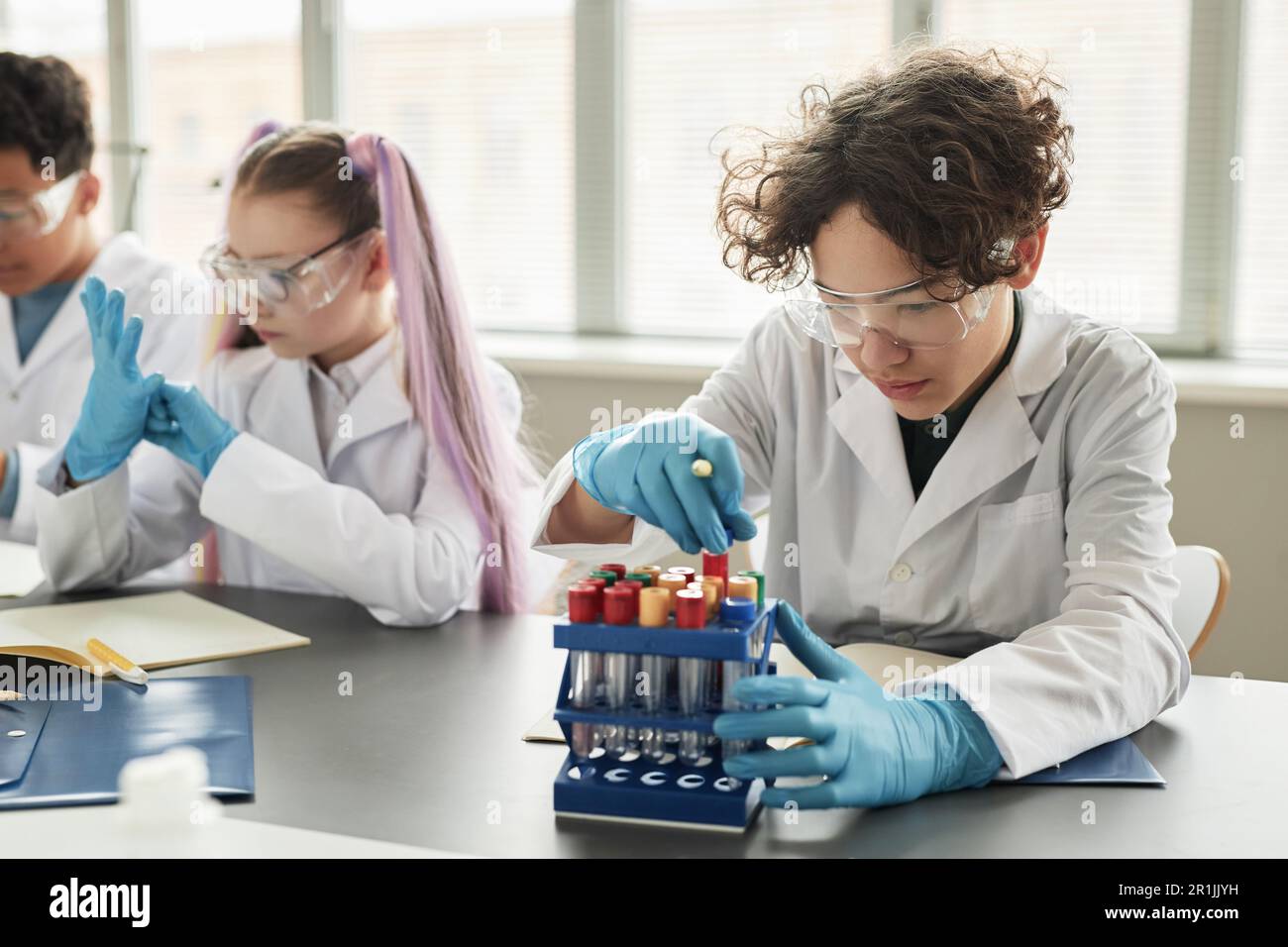 Porträt eines lockigen Teenager-Schülers, der im Wissenschaftsunterricht Becher ansieht und Experimente genießt Stockfoto