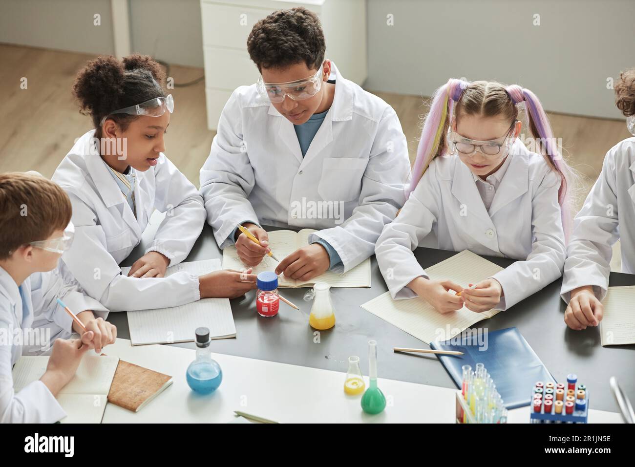 Draufsicht auf verschiedene Kindergruppen, die während des Wissenschaftskurses in der Schule Experimente durchführen und Labormäntel tragen Stockfoto