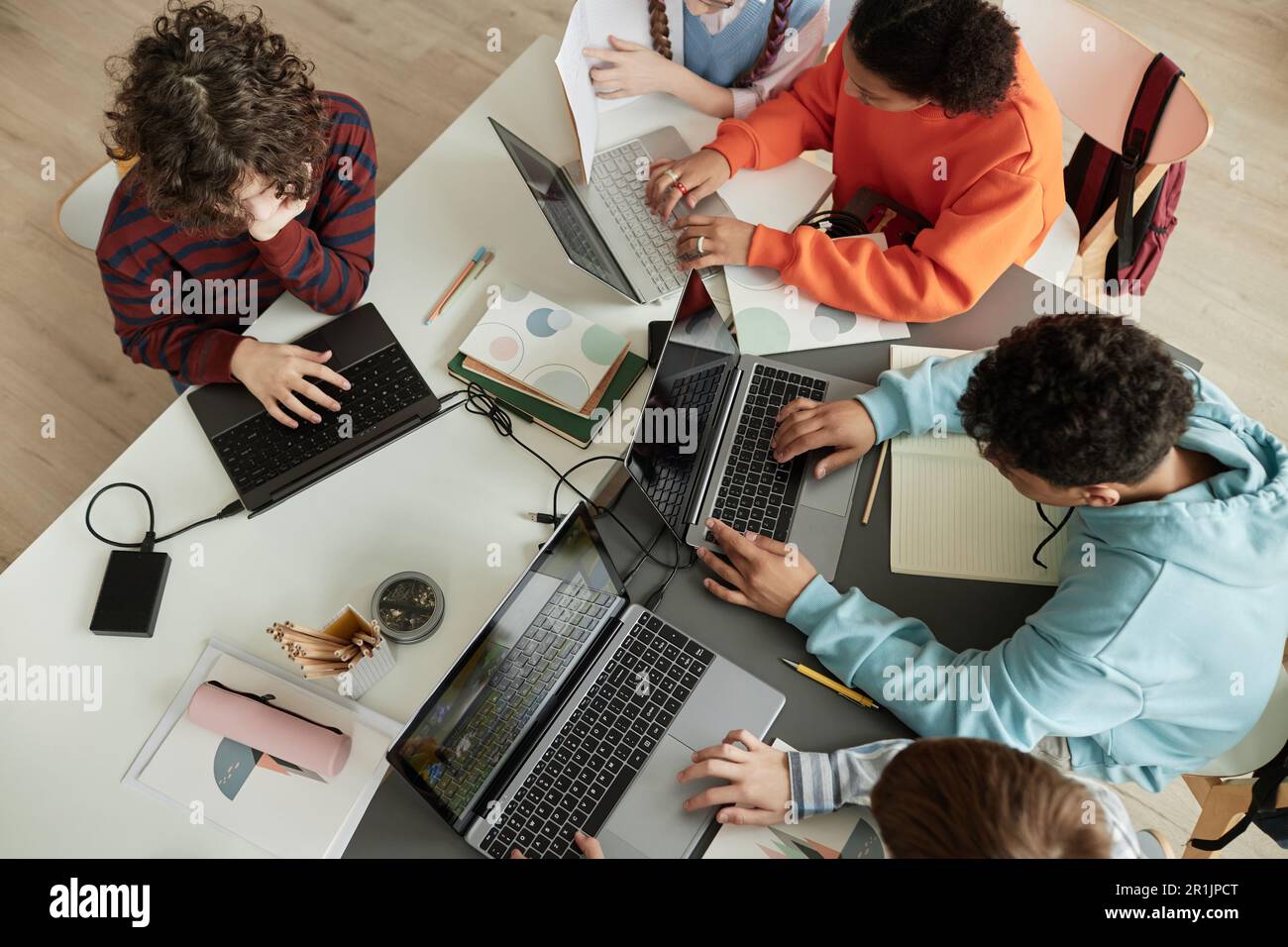 Draufsicht auf eine vielfältige Gruppe von Teenagern, die Computer im Klassenzimmer benutzen und gemeinsam am Tisch lernen Stockfoto