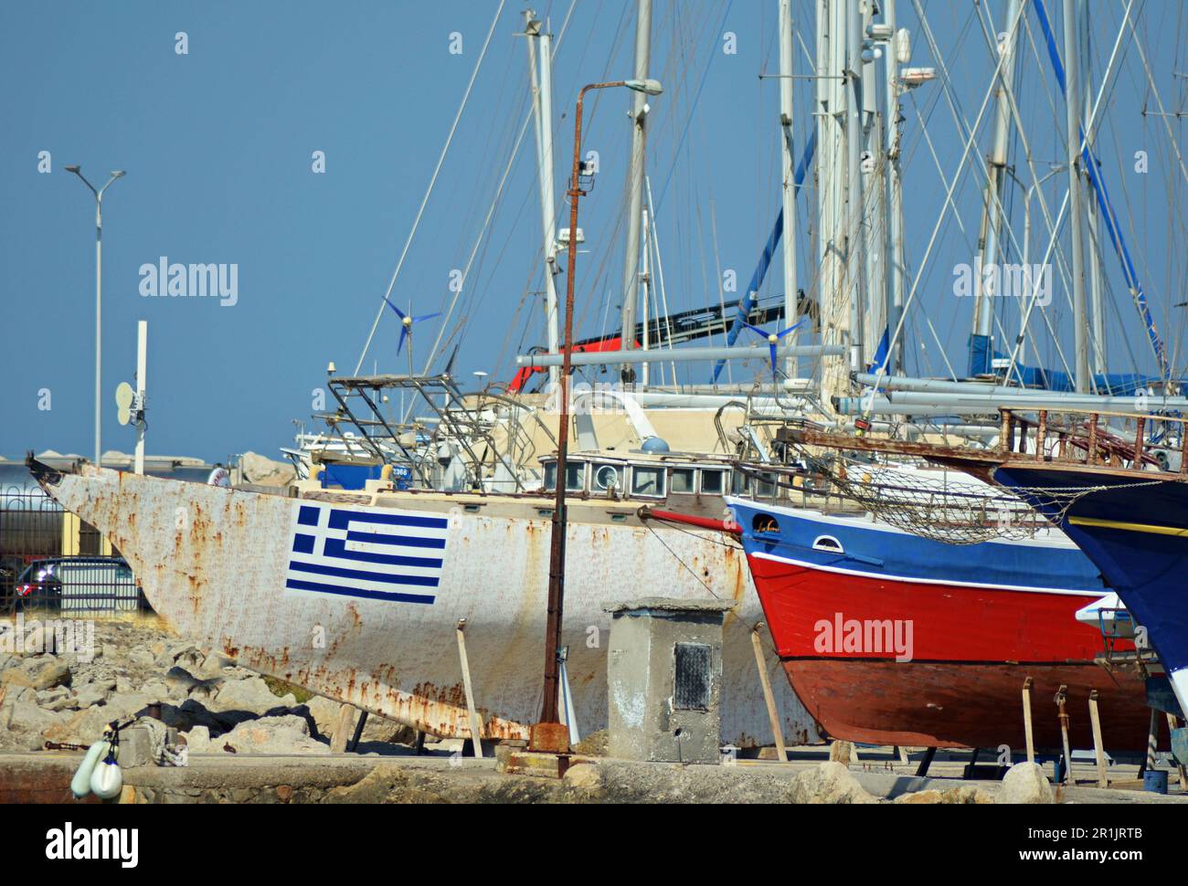 Schiffsdock, wo Schiffe mit Masten repariert werden. Auf einem der weißen Schiffe ist eine griechische Flagge gemalt. Das andere Schiff ist blau und rot. Stockfoto