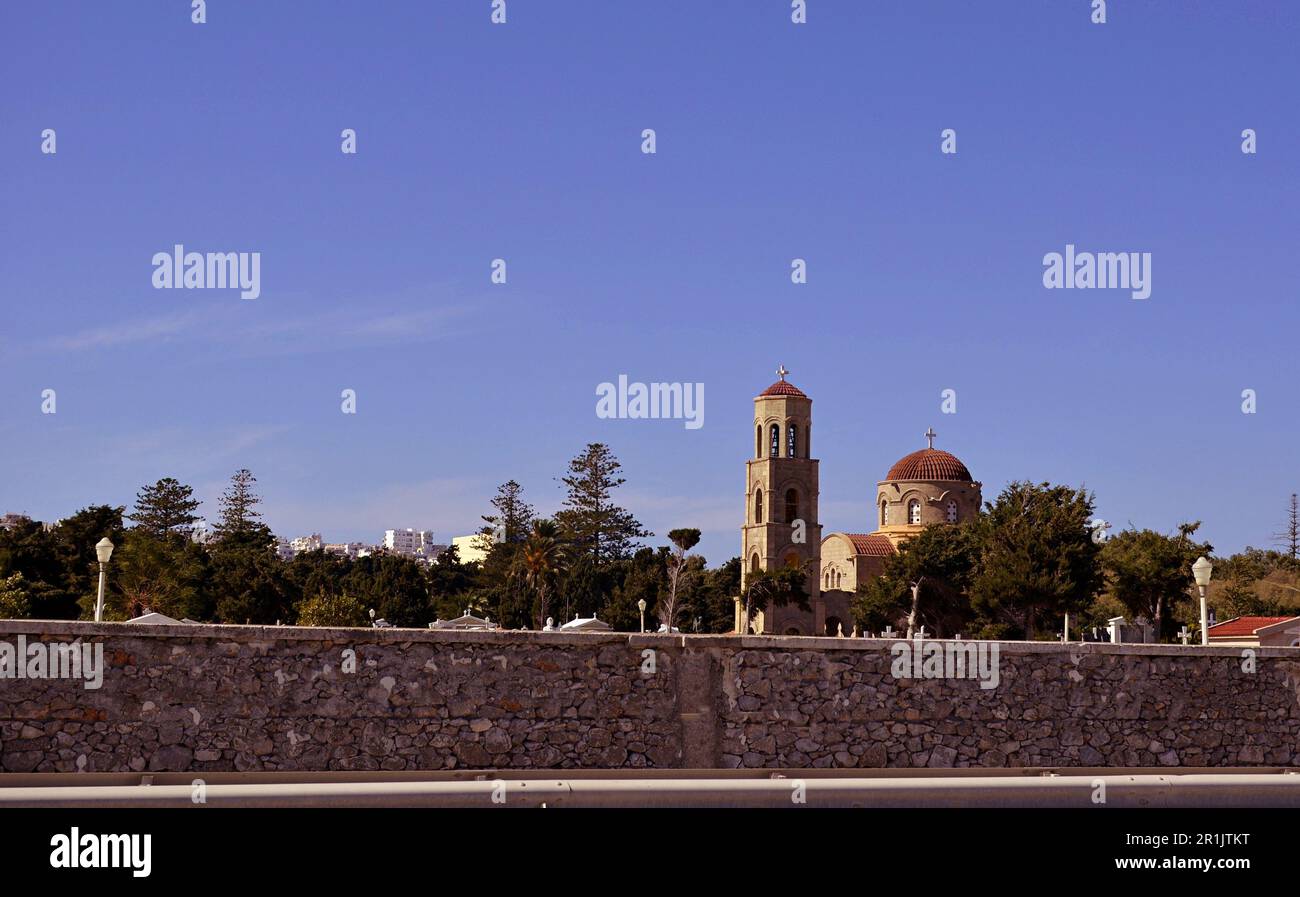 Byzantinische christliche Kirche mit einer runden gekachelten Kuppel und einem Glockenturm. Die Kirche befindet sich hinter einem Zaun. Hohe grüne Bäume um den Tempel Stockfoto