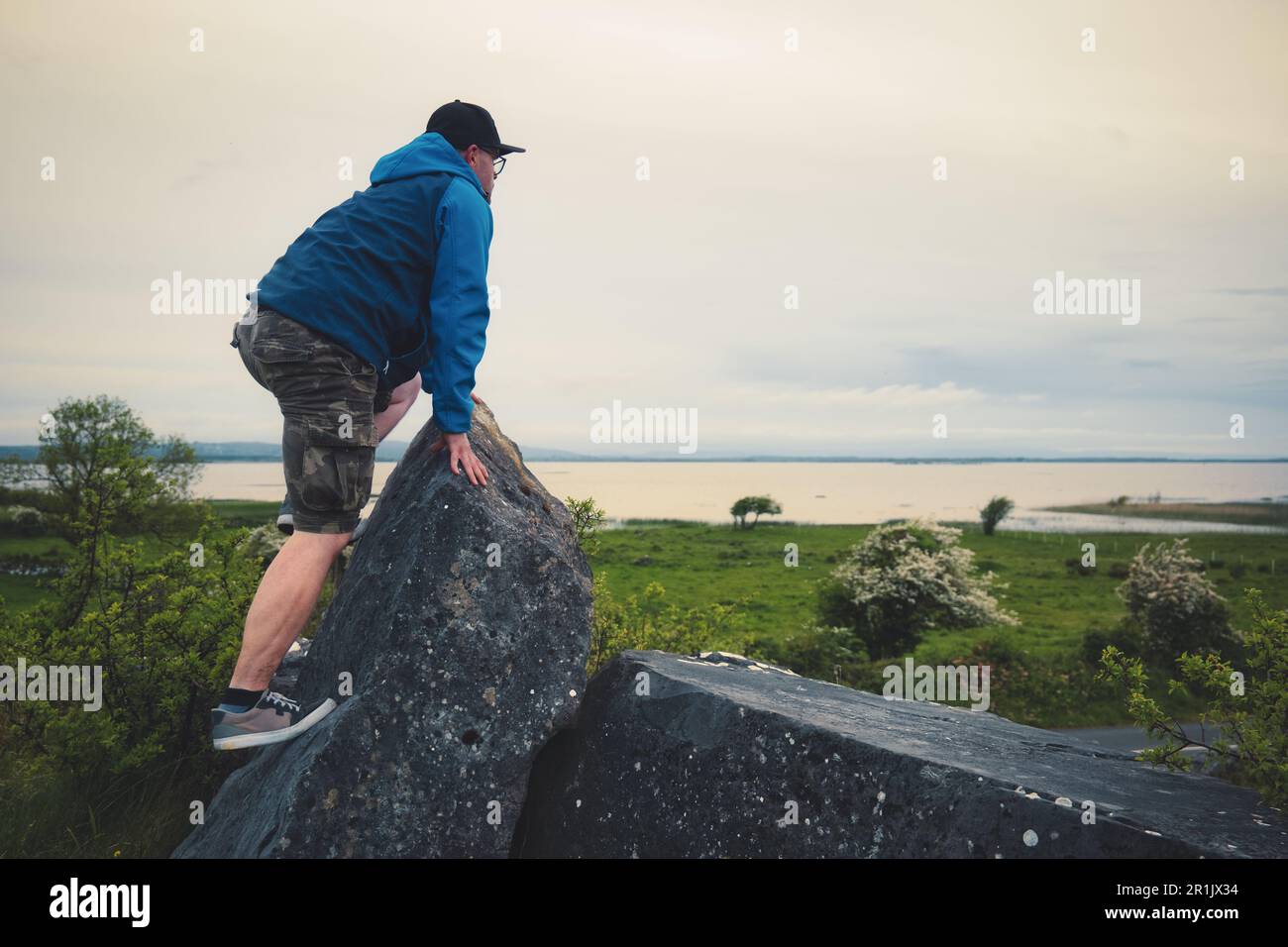 Mann klettert auf den Felsen auf dem grünen Hügel mit atemberaubendem Blick auf den Corrib See in Galway, Irland Stockfoto