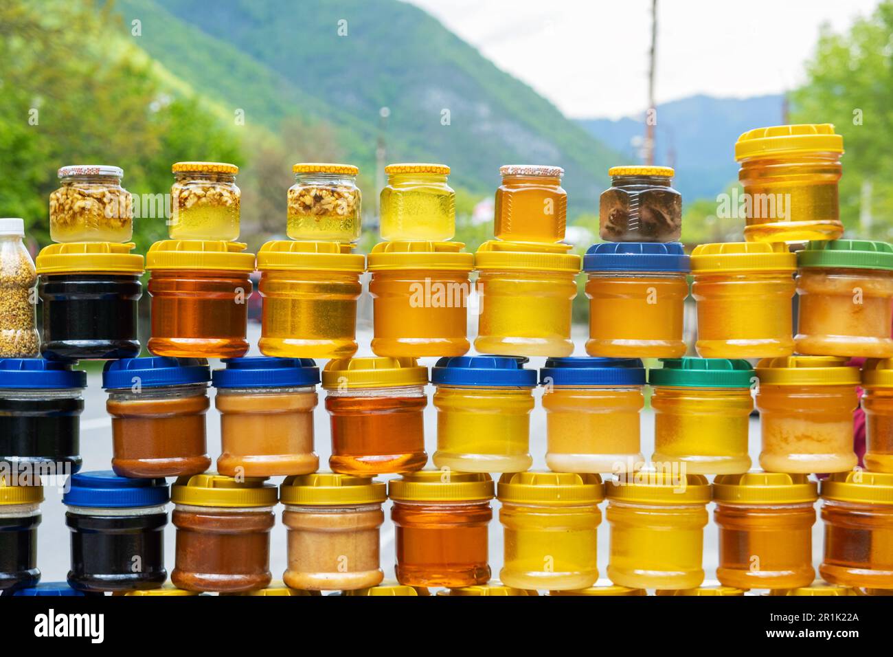Gläser mit Bio-Honig auf der Theke zum Verkauf im Freien auf dem georgischen Markt. Verschiedene Honigsorten, verschiedene Farben in Kunststoffdosen Stockfoto