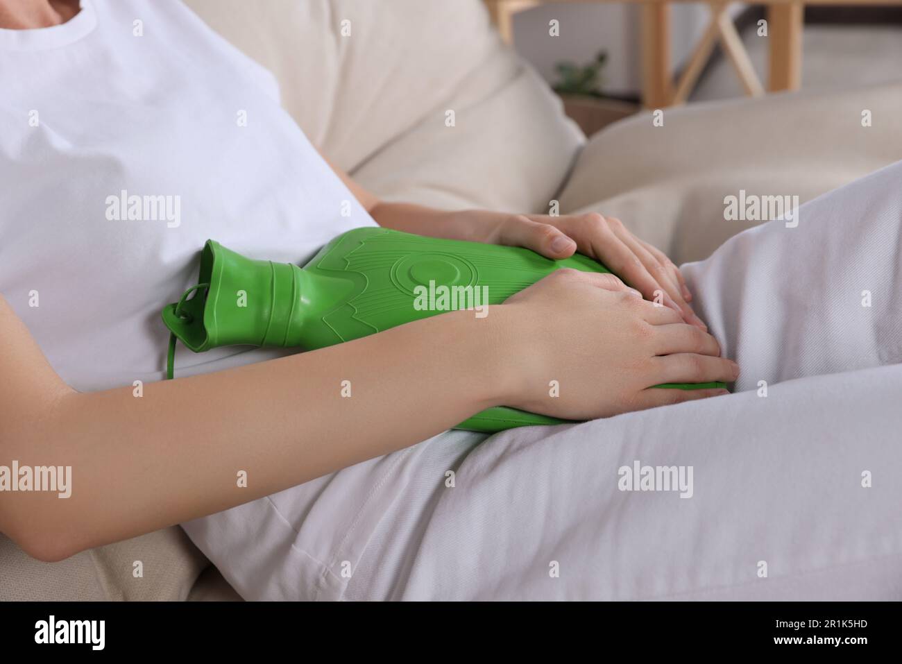 Frau, die eine Wärmflasche benutzt, um Zystitis-Schmerzen zu lindern, auf dem Sofa zu Hause, Nahaufnahme Stockfoto