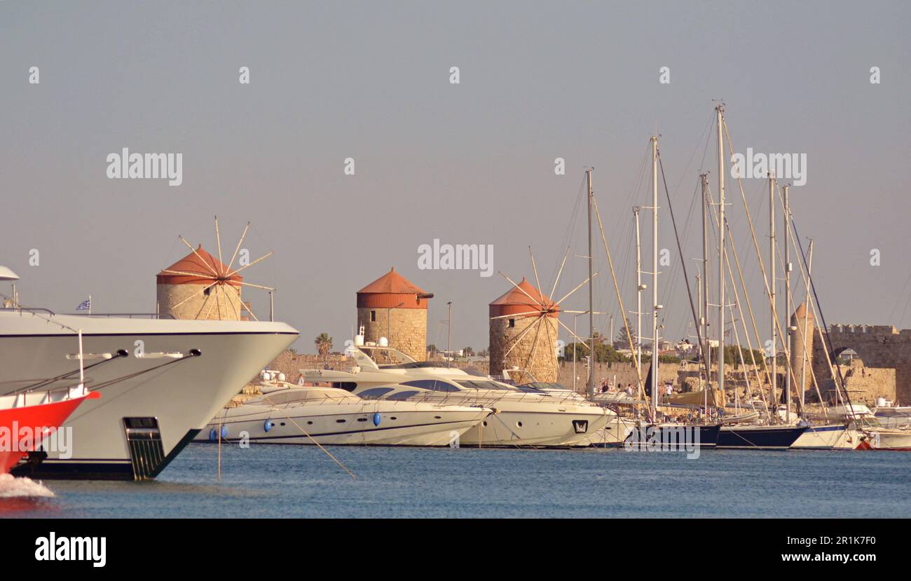 Mittelalterliche Steinmühlen mit roten Dächern im Hafen von Rhodos. Motor- und Segelyachten liegen am Ufer in Mandraki Bay vor. Stockfoto