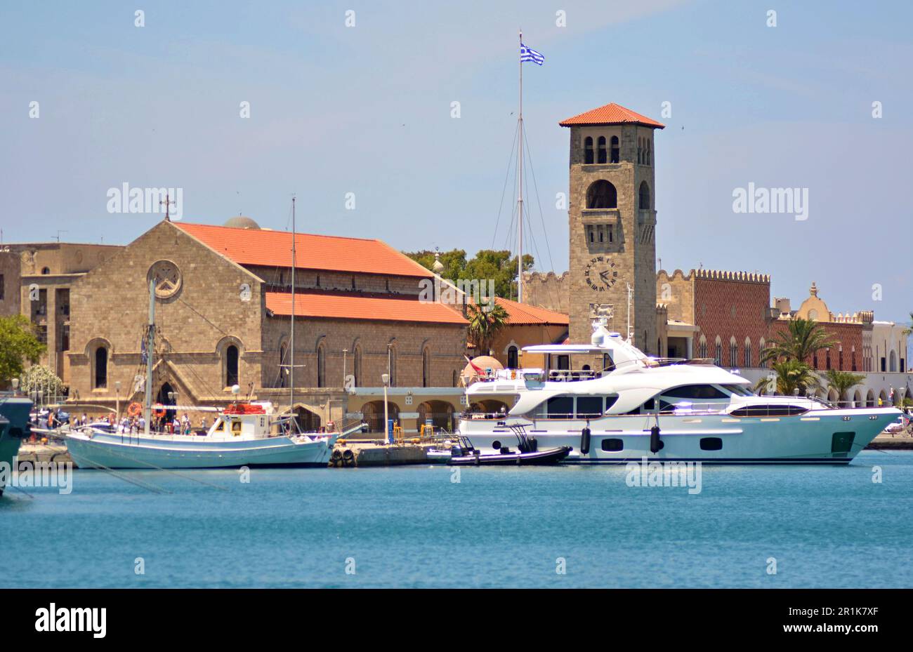 Seehafen Mandraki auf Rhodos mit gotischem Tempel und Glockenturm, rotem Dach, Sandsteinwänden. Motoryachten und Boote sind vor Anker. Stockfoto