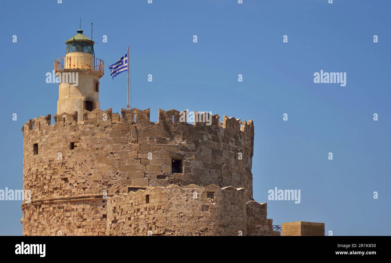 Nahaufnahme eines mittelalterlichen Leuchtturms aus Sandstein mit einer blau-weißen griechischen Flagge, die auf dem Gipfel weht. Turmbefestigungen vor dem blauen Himmel Stockfoto