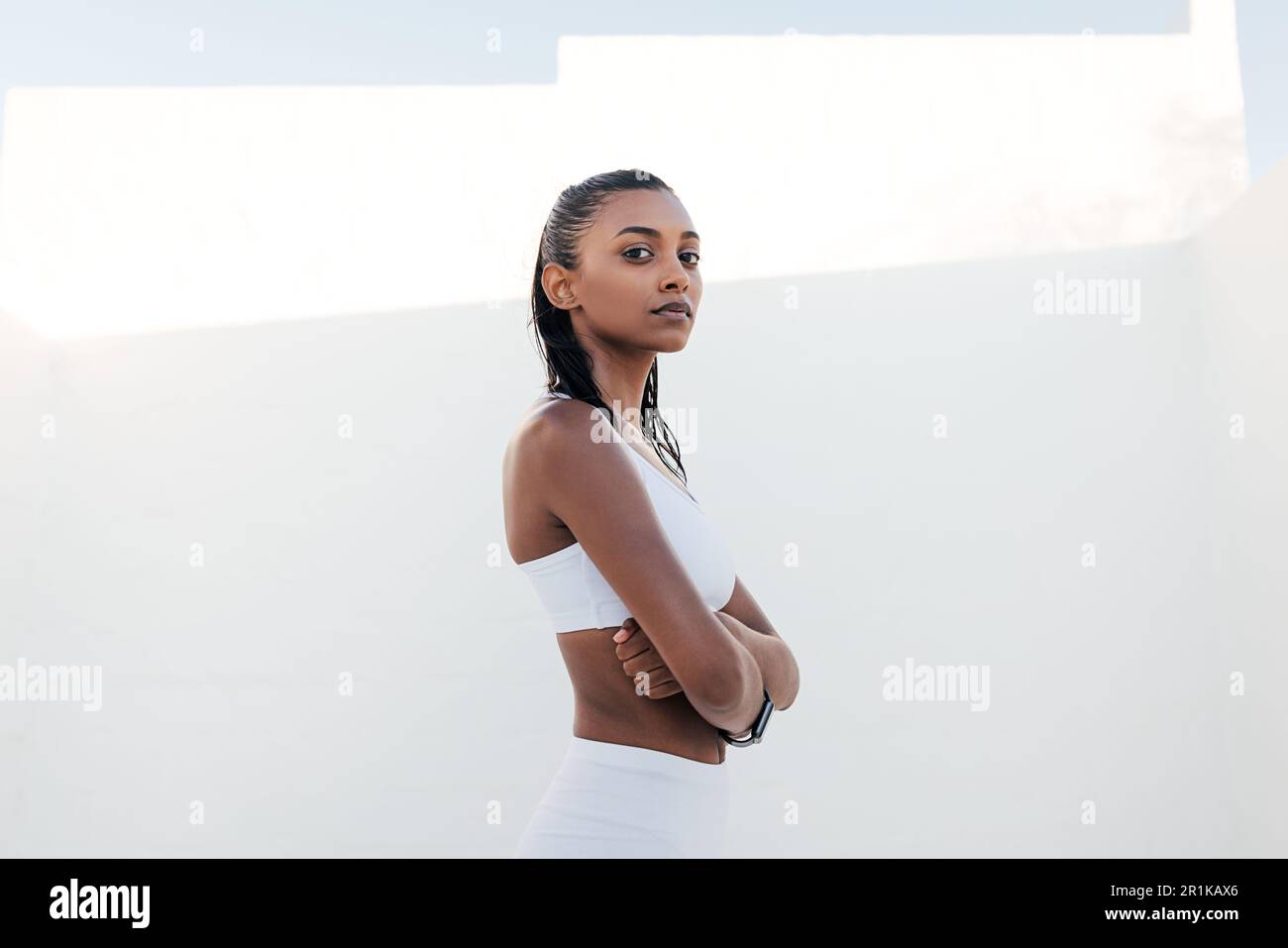 Selbstbewusste Frau in einem weißen Sport-BH, die mit gekreuzten Händen in die Kamera schaut Stockfoto